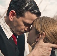 a man and woman kissing each other in front of a building with the sky behind them