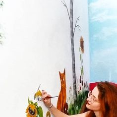 a woman is painting on the wall with sunflowers