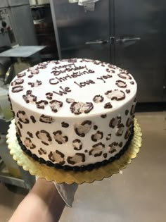 a person holding up a cake with white frosting and brown leopard print on it