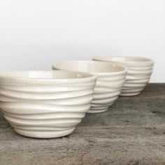 three white bowls sitting on top of a wooden table