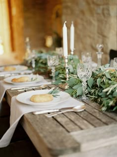 the table is set with white plates and silverware, greenery on each plate