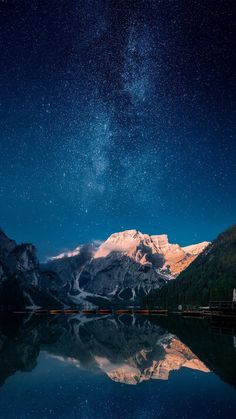 the night sky is reflected in water with mountains and trees around it, as well as stars above