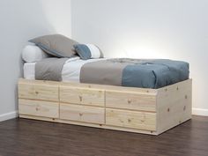 a bed with two drawers underneath it on the floor next to a white wall and hardwood floors