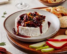 a cheese dish with fruit and crackers on a wooden platter next to wine glasses