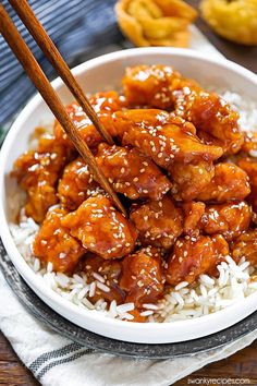 a white bowl filled with chicken and rice next to chopsticks on top of it