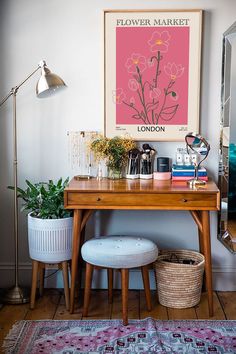 a wooden desk topped with a plant next to a white chair and a painting on the wall