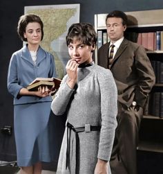 three people standing next to each other in front of bookshelves and a map