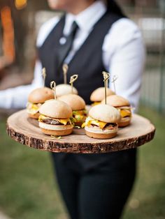 a person holding a tray with mini burgers on it