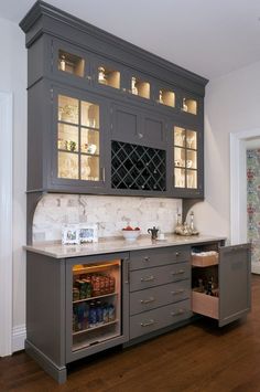 a kitchen with gray cabinets and white marble counter tops, an open wine cooler in the center