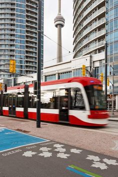 a red and white train traveling past tall buildings on a street next to a crosswalk