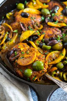 a skillet filled with chicken, olives and peppers on top of a table