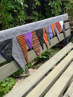 a wooden bench sitting in front of a forest filled with trees and bushes next to a row of colorful ties