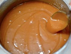 an orange sauce in a silver pot with a wooden spoon sticking out of the top