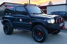 a black jeep parked in front of a building with the sun setting on it's roof