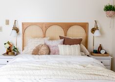 a bed with pillows and blankets on top of it next to two nightstands filled with plants