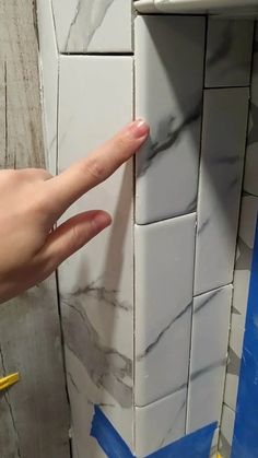 a person's hand pointing at a white tile wall