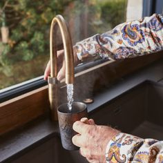 a person is pouring water from a faucet into a cup in front of a window