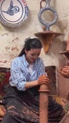 a woman sitting on the ground next to a clay pot and another person standing near her