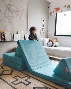 a little boy sitting on top of a blue bed in a room with white walls