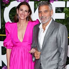 a man and woman standing next to each other in front of a flower covered wall