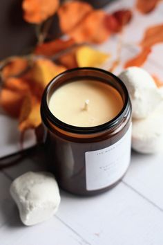 a candle sitting on top of a white table next to some pumpkins and leaves