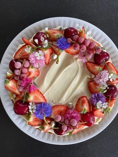 a white plate topped with a cake covered in strawberries and other fruit toppings