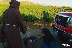 two men in costumes are talking to each other near a red pickup truck and vineyard