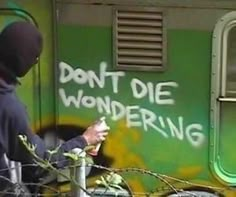 a man in a hoodie writing on the side of a green and yellow train