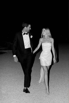 a man in a tuxedo walking next to a woman in a white dress