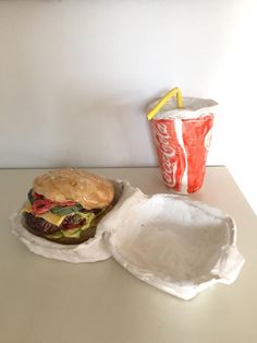 a plastic container with a hamburger and a soda cup on the table next to it