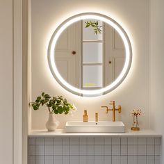 a bathroom sink with a round mirror above it and a vase filled with flowers on the counter