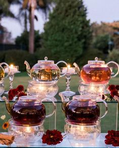 glass teapots with lit candles and flowers in them on a clear table outside