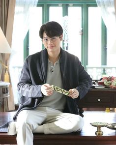 a young man sitting on top of a wooden table holding a tie in his hand