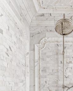 a shower head in a white bathroom with marble walls and floor tiles on the wall