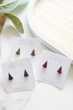 three small red and black triangle studs on top of a white card next to green leaves