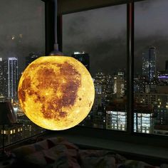 a full moon lamp hanging from the ceiling in front of a window with city lights