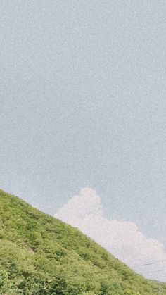 two people standing on the side of a hill flying a kite in the sky above them