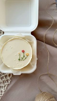 a white box with flowers on it sitting on a lace tablecloth next to some twine