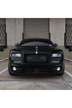 the front end of a black rolls royce parked in a parking lot next to garage doors