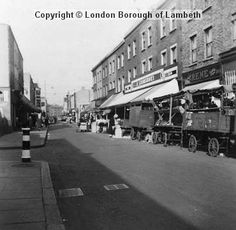 an old black and white photo of people standing on the side of a road near buildings