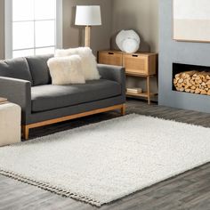 a living room with a gray couch and white rugs on the wooden flooring