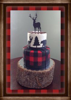 a three tiered cake decorated with black and red plaid, moose, and trees