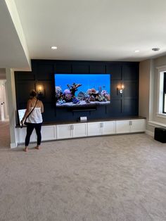 a woman standing in front of a flat screen tv next to a wall mounted fish tank