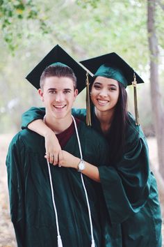 two young people in graduation gowns hugging each other and smiling at the camera with trees behind them