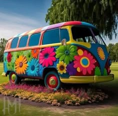 a colorful bus is parked in the middle of a flower bed with trees and grass behind it