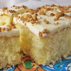 a piece of cake with white frosting and nuts on top is sitting on a colorful plate