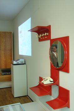 there is a red shelf with a mirror on it and a phone in the foreground