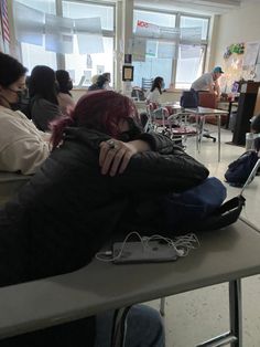 two people hugging each other while sitting at desks in a room with tables and chairs