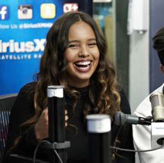 two people sitting in front of microphones with one person smiling and the other laughing