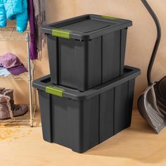 two black storage containers sitting on top of a wooden floor next to a coat rack